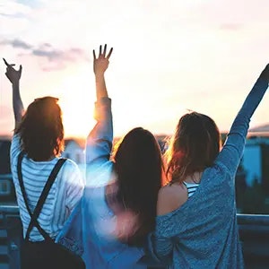 three young adult females with their hands raised looking out at horizon