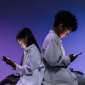 two children sitting back to back staring at thier phones